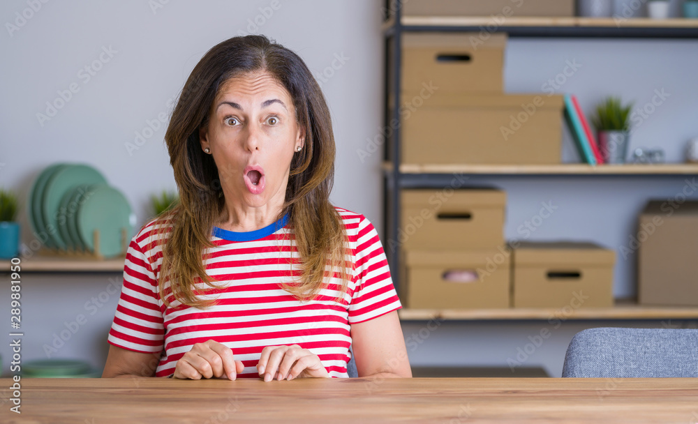 Middle age senior woman sitting at the table at home afraid and shocked with surprise and amazed expression, fear and excited face. Middle age senior woman sitting at the table at home afraid and shocked with surprise and amazed expression, fear and excited face.