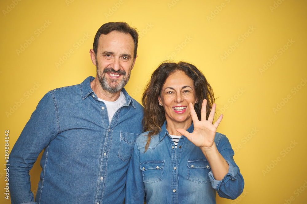 Beautiful middle age couple together standing over isolated yellow background showing and pointing up with fingers number five while smiling confident and happy. Beautiful middle age couple together standing over isolated yellow background showing and pointing up with fingers number five while smiling confident and happy.