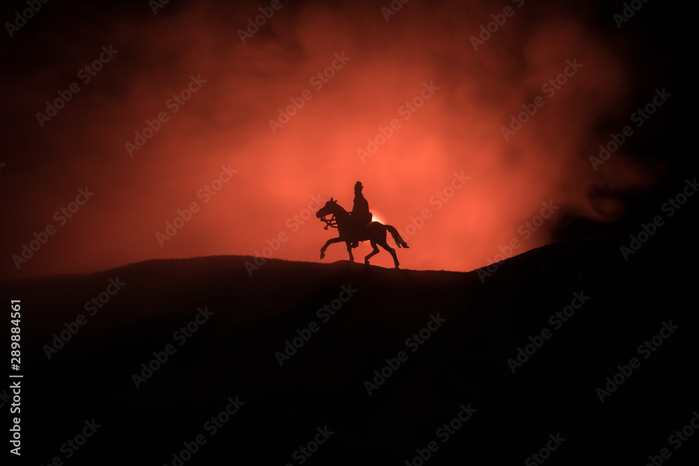 World war officer (or warrior) rider on horse with a sword ready to fight and soldiers on a dark foggy toned background. Battle scene battlefield of fighting soldiers.