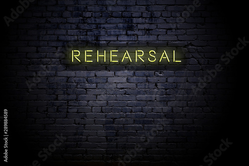 Highlighted brick wall with neon inscription rehearsal