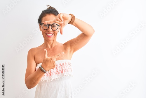 Middle age woman wearing casual dress and glasses standing over isolated white background smiling making frame with hands and fingers with happy face. Creativity and photography concept.