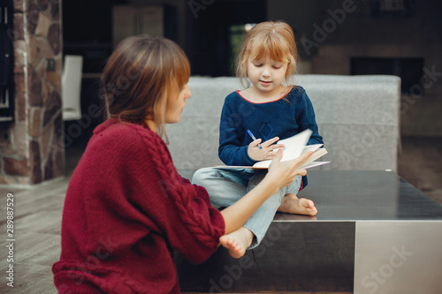 Beautiful mother with little daughter. Family sitting in the room. Cute girl doing homework photo