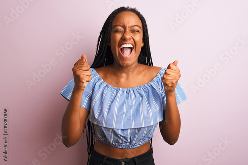 African american woman wearing striped t-shirt standing over isolated pink background excited for success with arms raised and eyes closed celebrating victory smiling. Winner concept.