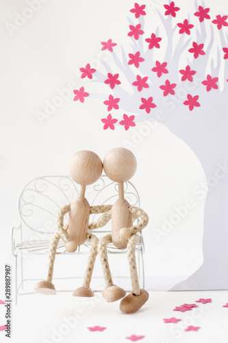 Two figurines sitting on a bench under a paper cherry tree and hug each other portrait format