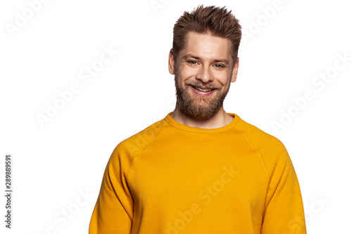 Cute guy in a stylish bright sweatshirt stands on an isolated white background and smiling looks at the camera