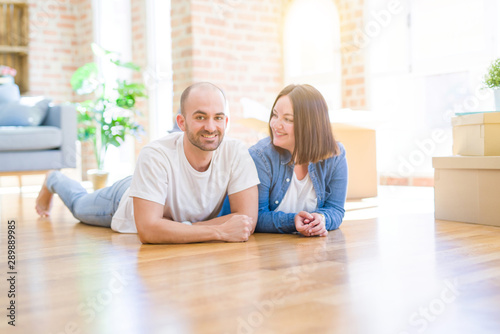 Young couple in love lying on the floor of new house arround cardboard boxes, smiling very happy for moving to a new apartment