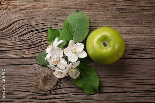 Ripe green apple with branch of white flowers on a wooden table