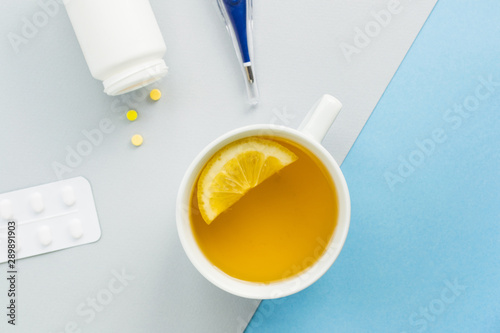 Cold and flu season. Cup with hot tea and lemon, thermometer, pills on a light background. Treatment and prevention of the virus. Copy space