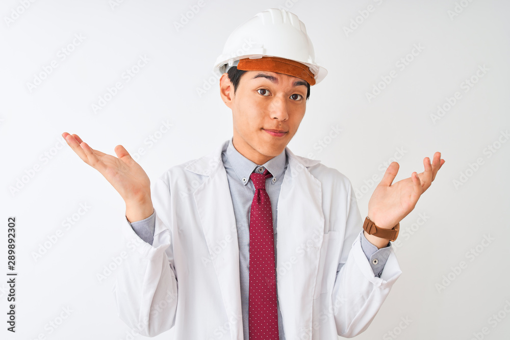 Chinese architect man wearing coat and helmet standing over isolated white background clueless and confused expression with arms and hands raised. Doubt concept. Chinese architect man wearing coat and helmet standing over isolated white background clueless and confused expression with arms and hands raised. Doubt concept.