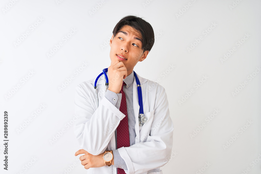 Chinese doctor man wearing coat tie and stethoscope over isolated white background with hand on chin thinking about question, pensive expression. Smiling with thoughtful face. Doubt concept. Chinese doctor man wearing coat tie and stethoscope over isolated white background with hand on chin thinking about question, pensive expression. Smiling with thoughtful face. Doubt concept.