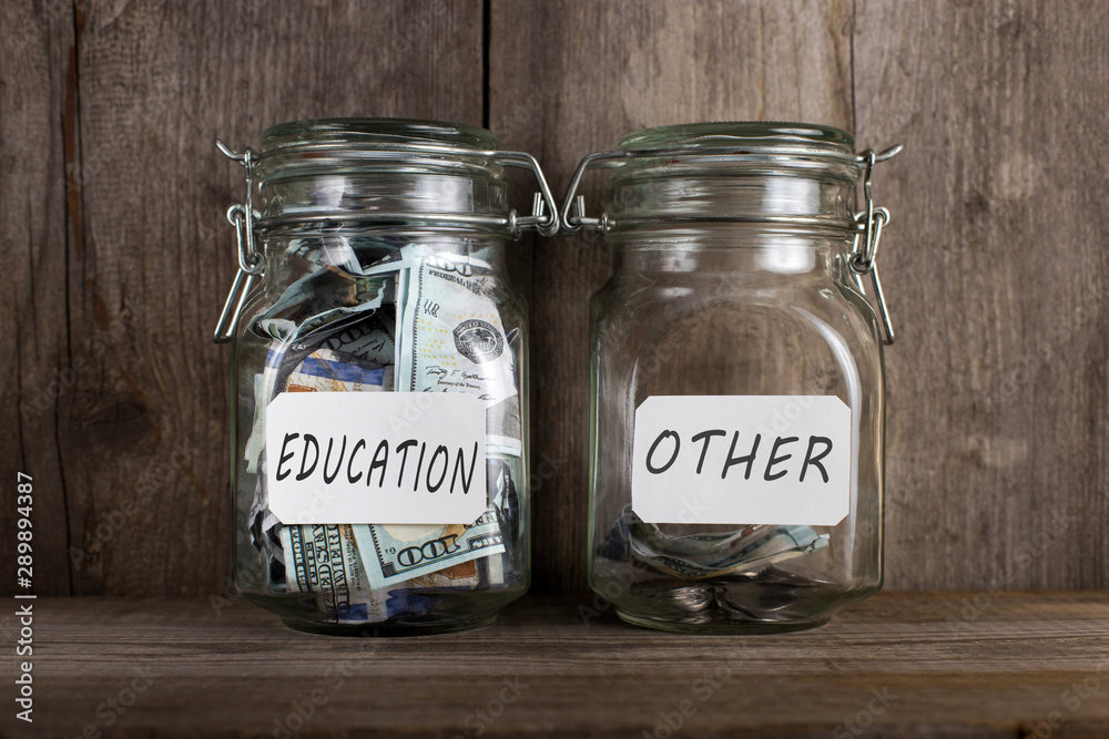 Two piggy banks, with different amounts of money and space for text, stand on a wooden bookshelf. Two piggy banks, with different amounts of money and space for text, stand on a wooden bookshelf.