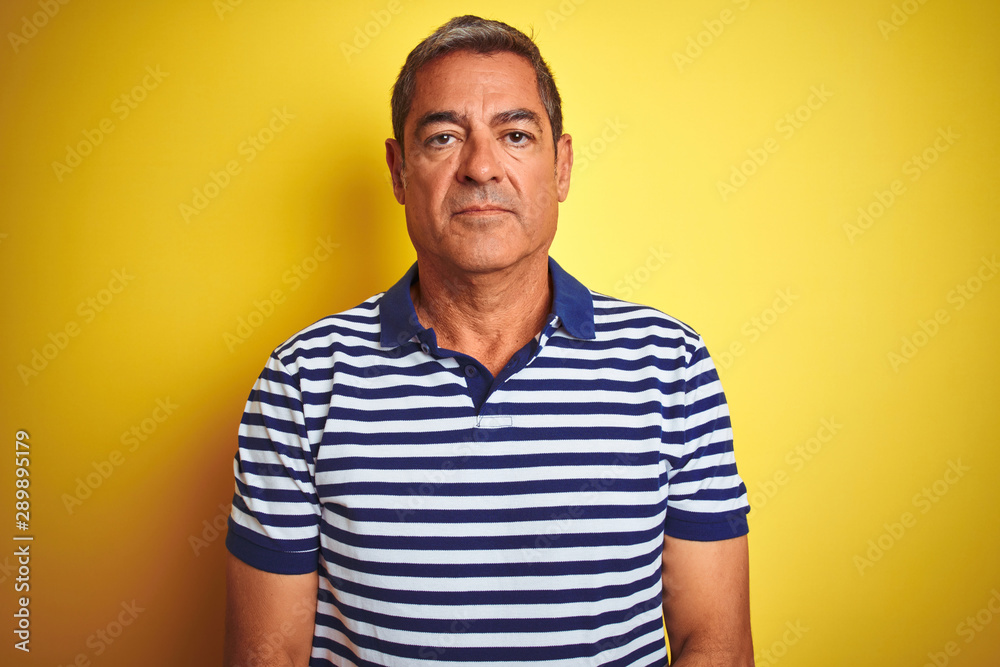 Handsome middle age man wearing striped polo standing over isolated yellow background with serious expression on face. Simple and natural looking at the camera. - obrazy, fototapety, plakaty 