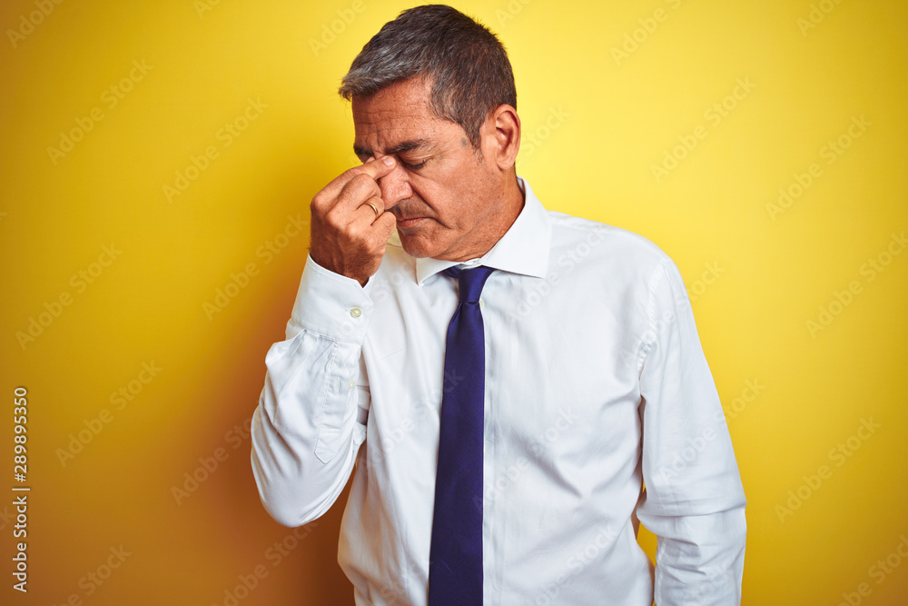 Handsome middle age businessman standing over isolated yellow background tired rubbing nose and eyes feeling fatigue and headache. Stress and frustration concept.
