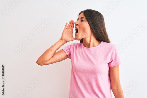 Young beautiful woman wearing pink casual t-shirt standing over isolated white background shouting and screaming loud to side with hand on mouth. Communication concept.