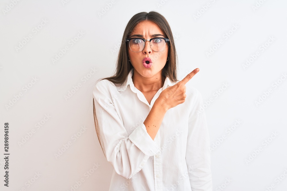 Young beautiful businesswoman wearing glasses standing over isolated white background Surprised pointing with finger to the side, open mouth amazed expression. Young beautiful businesswoman wearing glasses standing over isolated white background Surprised pointing with finger to the side, open mouth amazed expression.