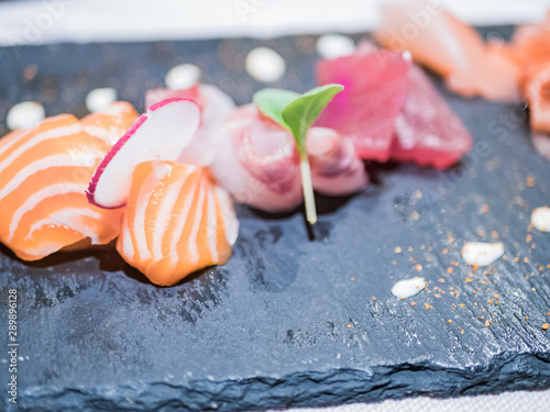 Typical Japanese dish of sushimi with tuna salmon roll on a black background.