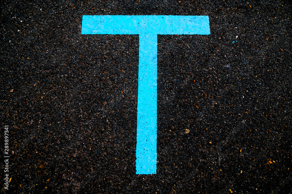 Letter T, blue sign in reflective paint on asphalt.