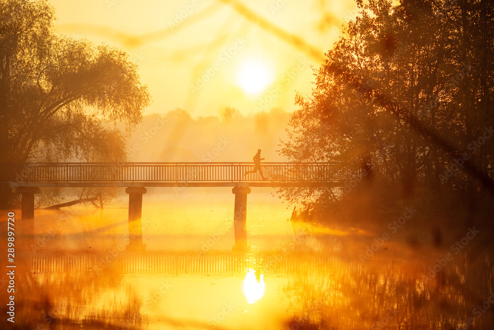 Man is running across bridge at sunrise.
