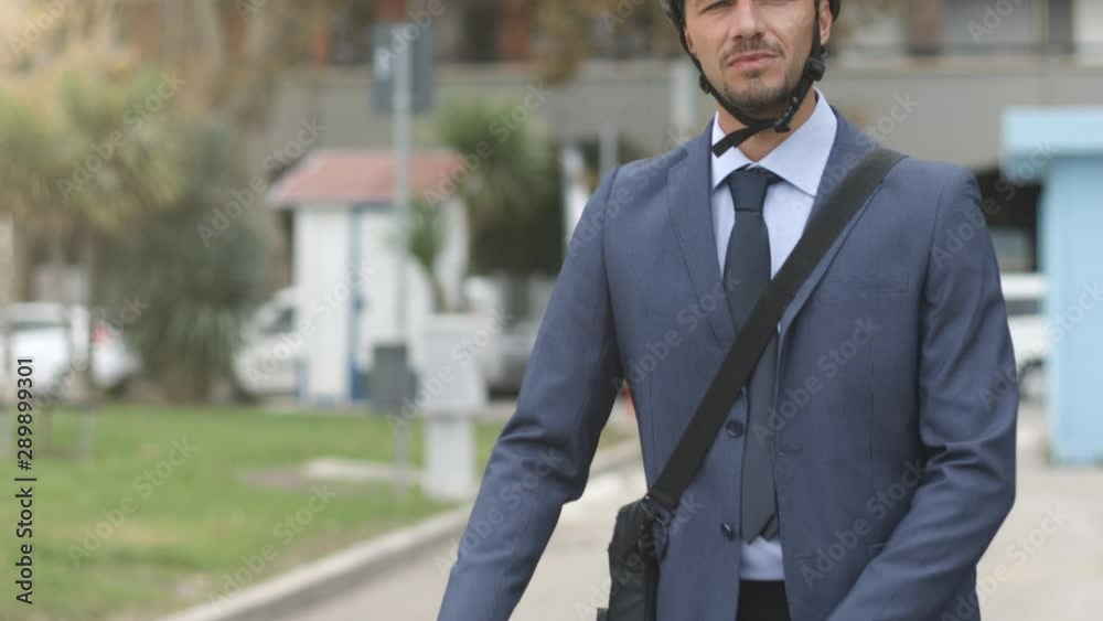 Amazing tracking shot tilt down portrait of handsome young businessman with a briefcase on the shoulder and a bike helmet pushing his bike in the city at sunrise or sunset. Amazing tracking shot tilt down portrait of handsome young businessman with a briefcase on the shoulder and a bike helmet pushing his bike in the city at sunrise or sunset.