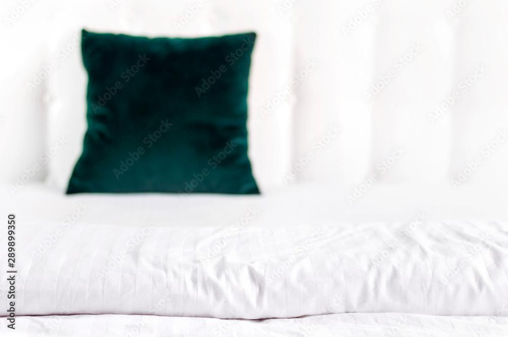 Bright decorative soft pillows in bed on the background of leather quilted headboard. Emerald and orange pillow, part of bed close-up, comfort. Quilted headboard background, interior