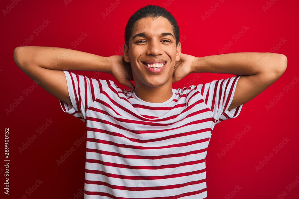 Young handsome arab man wearing striped t-shirt over isolated red background relaxing and stretching, arms and hands behind head and neck smiling happy Young handsome arab man wearing striped t-shirt over isolated red background relaxing and stretching, arms and hands behind head and neck smiling happy