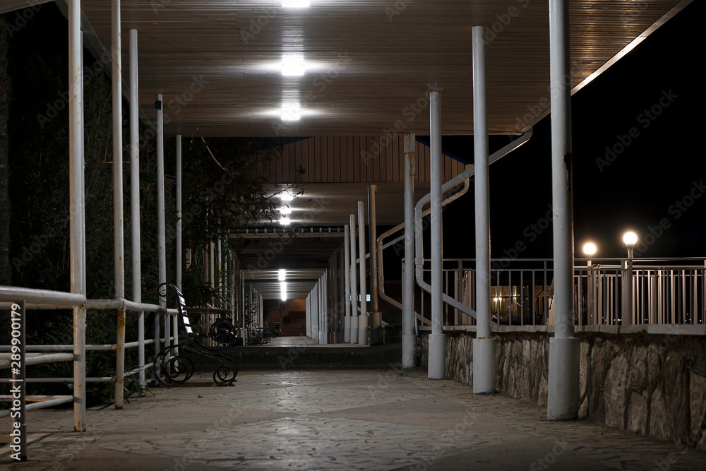 The modern structure of the corridor in the hotel in the open air. Street terrace at night with an iron bench and iron fence.