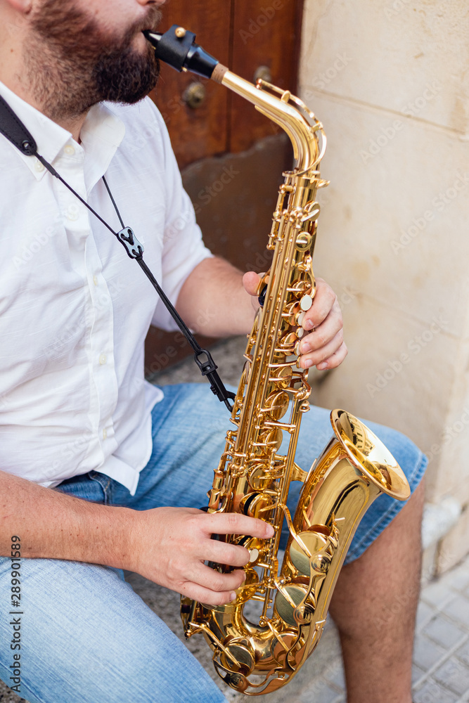 Naklejka premium Close up of a man sitting at the door of a building on the street holding his saxophone