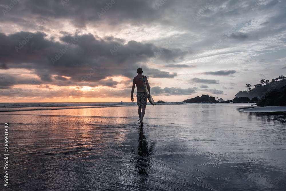 Hombre camina por la playa de colombia hacia el océano pacífico para surfear al atardecer. 