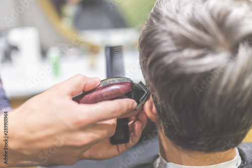 Barbershop. Hairdresser does hairstyle with hair clipper and comb.