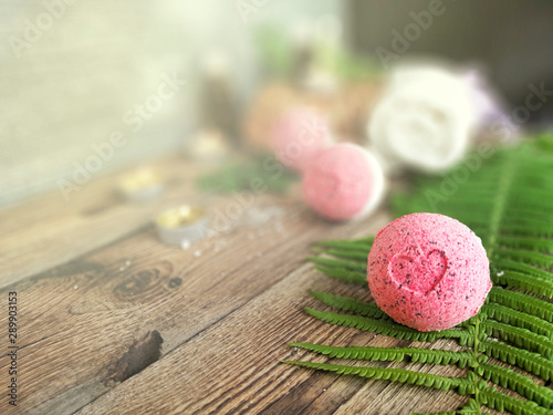 Pink bath bomb with fern leaf  on wooden background. Summer spa life style concept for vacation and relax. Selective focus.  Copy space.