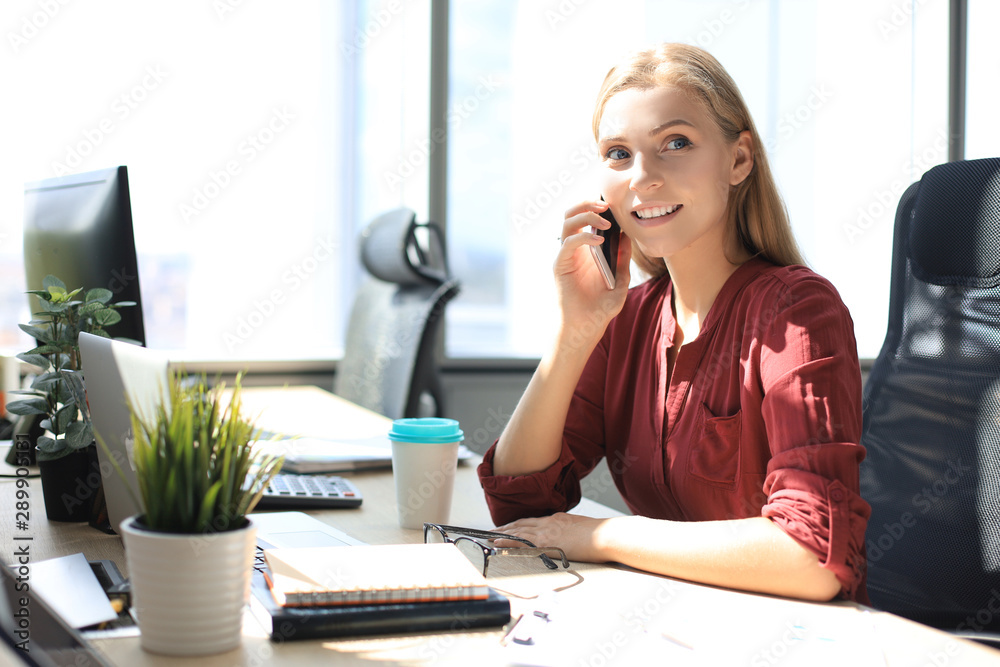Attractive business woman talking with collegues on the mobile phone while sitting in the office desk Attractive business woman talking with collegues on the mobile phone while sitting in the office desk