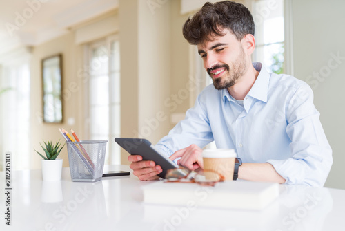 Young business man using touchpad tablet with a happy face standing and smiling with a confident smile showing teeth