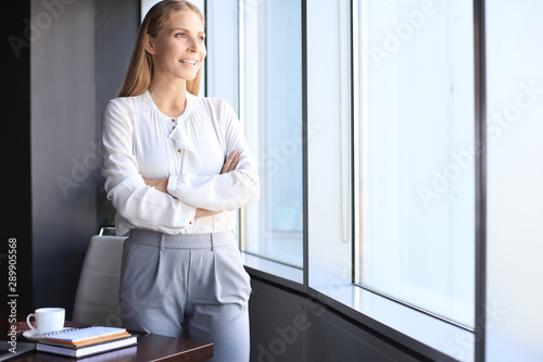 Attractive business woman looking at camera and smiling while standing in the office near the window