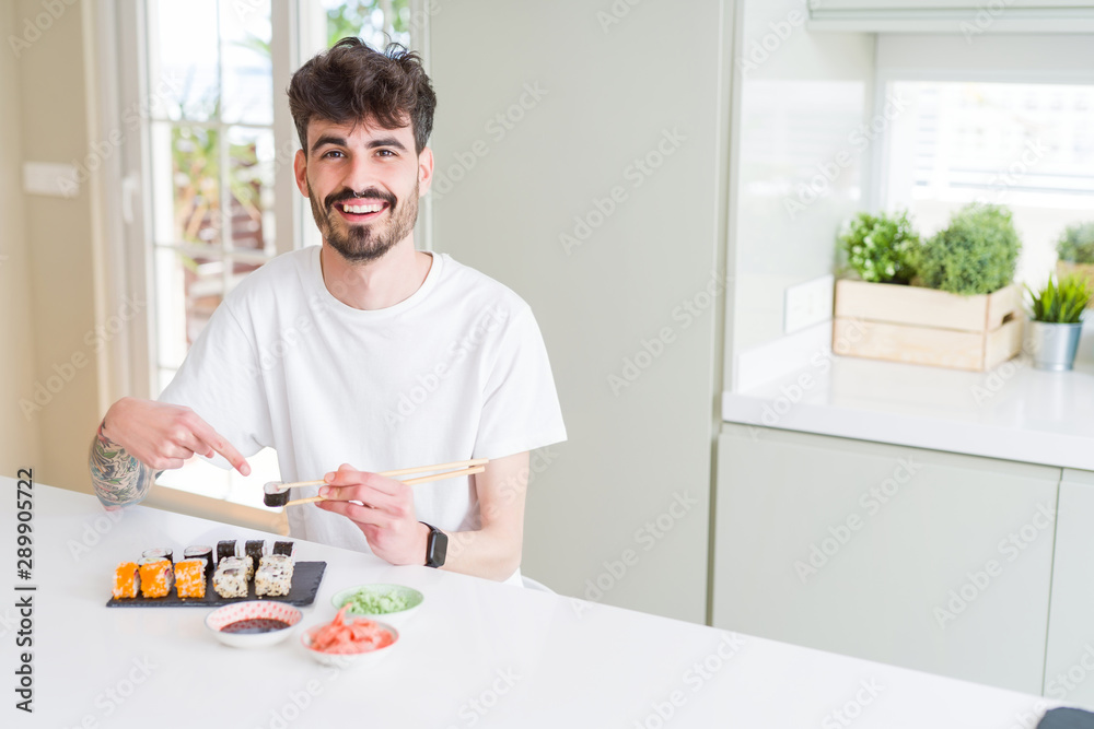 Young man eating asian sushi from home delivery very happy pointing with hand and finger Young man eating asian sushi from home delivery very happy pointing with hand and finger