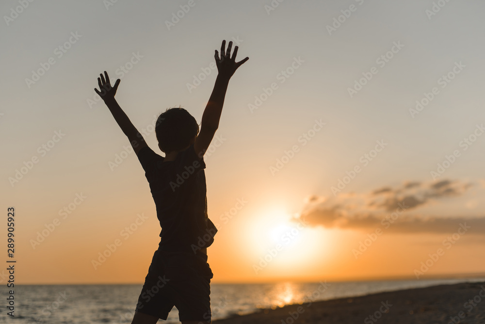 Silhouette of a joyful boy on a background of beach sunset.