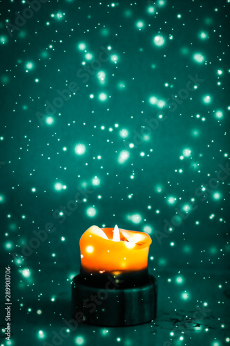 Canvas Print Orange holiday candle on green sparkling snowing background, luxury branding des