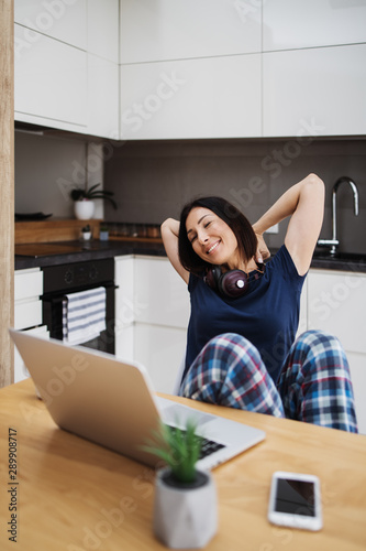 Attractive and happy middle age female freelancer is working and smiling at her home. Modern kitchen in background. Freelancing job concept.