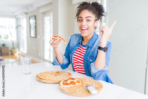 Young african american woman eating two homemade cheese pizzas very happy pointing with hand and finger to the side
