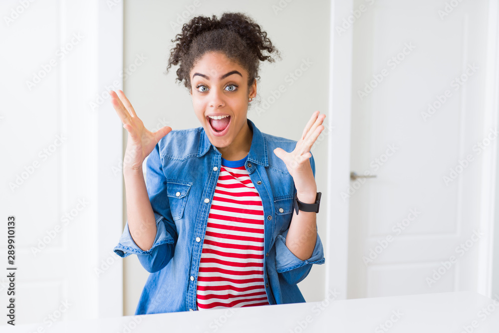 Beautiful young african american woman with afro hair wearing casual denim jacket celebrating crazy and amazed for success with arms raised and open eyes screaming excited. Winner concept