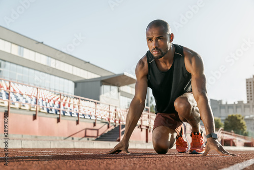 Fototapeta Naklejka Na Ścianę i Meble -  Low angle view of young man athlete in starting position for running on sports track