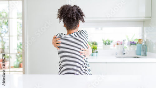Beautiful african american woman with afro hair wearing casual striped sweater Hugging oneself happy and positive from backwards. Self love and self care