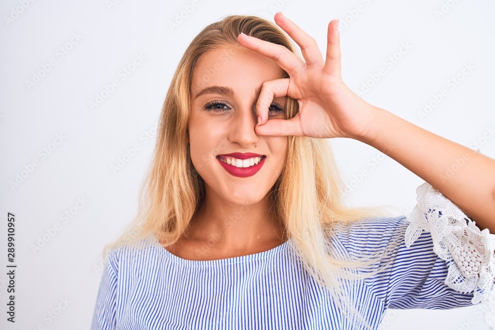 Young beautiful woman wearing elegant blue t-shirt standing over isolated white background with happy face smiling doing ok sign with hand on eye looking through fingers Young beautiful woman wearing elegant blue t-shirt standing over isolated white background with happy face smiling doing ok sign with hand on eye looking through fingers