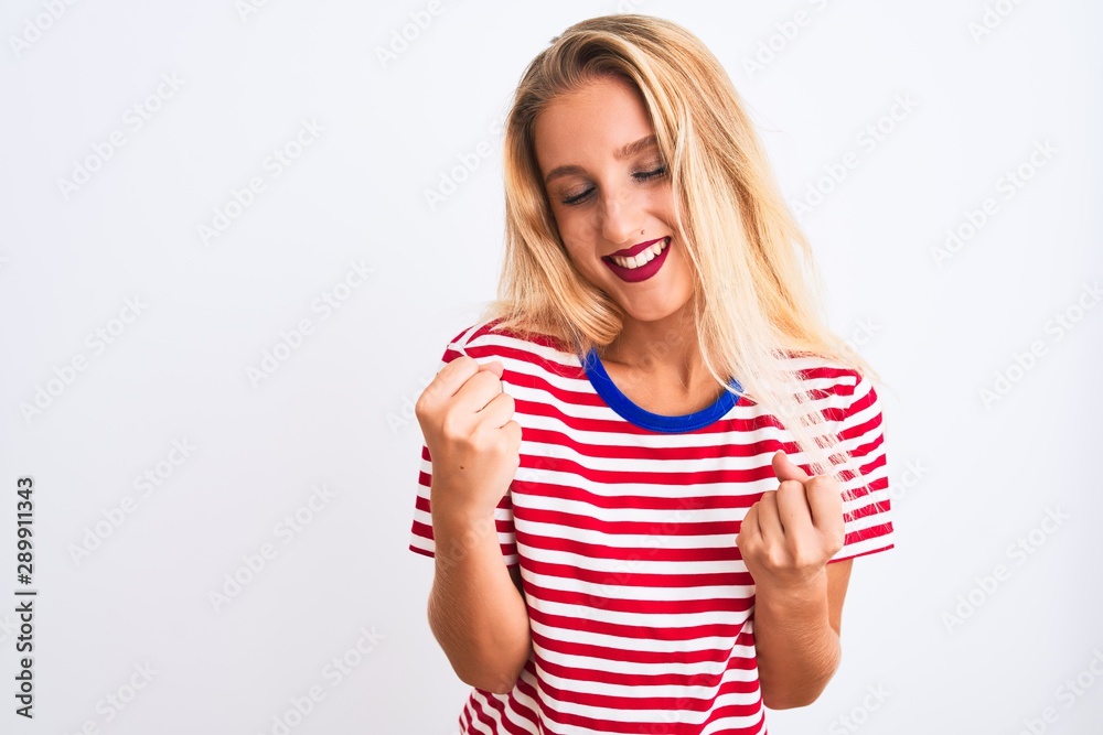 Young beautiful woman wearing red striped t-shirt standing over isolated white background very happy and excited doing winner gesture with arms raised, smiling and screaming for success. Young beautiful woman wearing red striped t-shirt standing over isolated white background very happy and excited doing winner gesture with arms raised, smiling and screaming for success.