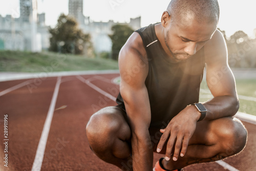 Portrait of tired african male athlete finished workout and resting while sitting on a racetrack
