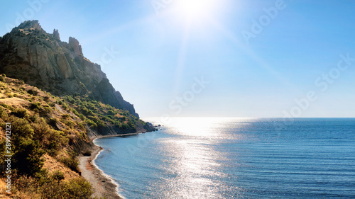 beautiful sea shore and vulcan rock mountain surrounded by ocean water panorama landscape view of Karadag mountain in Crimea with sun reflection on black sea surface natural color of nature scenery photo