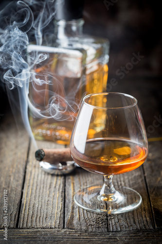 Glass and a bottle of brandy or cognac and smoking cigar on the wooden table.