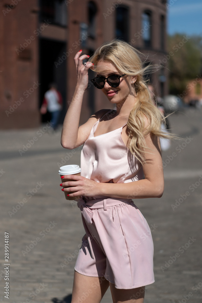 beautiful blonde girl walks around city with glass take-away coffee. Resting, sunny day beautiful blonde girl walks around city with glass take-away coffee. Resting, sunny day