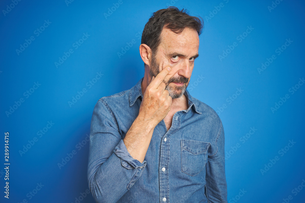 Handsome middle age senior man with grey hair over isolated blue background Pointing to the eye watching you gesture, suspicious expression Handsome middle age senior man with grey hair over isolated blue background Pointing to the eye watching you gesture, suspicious expression