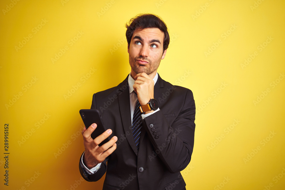 Young handsome businessman using smartphone standing over isolated yellow background serious face thinking about question, very confused idea Young handsome businessman using smartphone standing over isolated yellow background serious face thinking about question, very confused idea