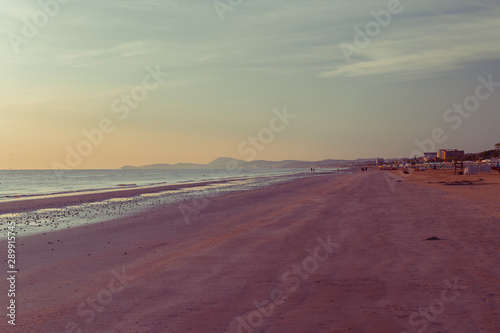 Sunset on the beach. Tinted photo in golden highlights. Sea and sandy beach. Banner, long format. Free space for text.